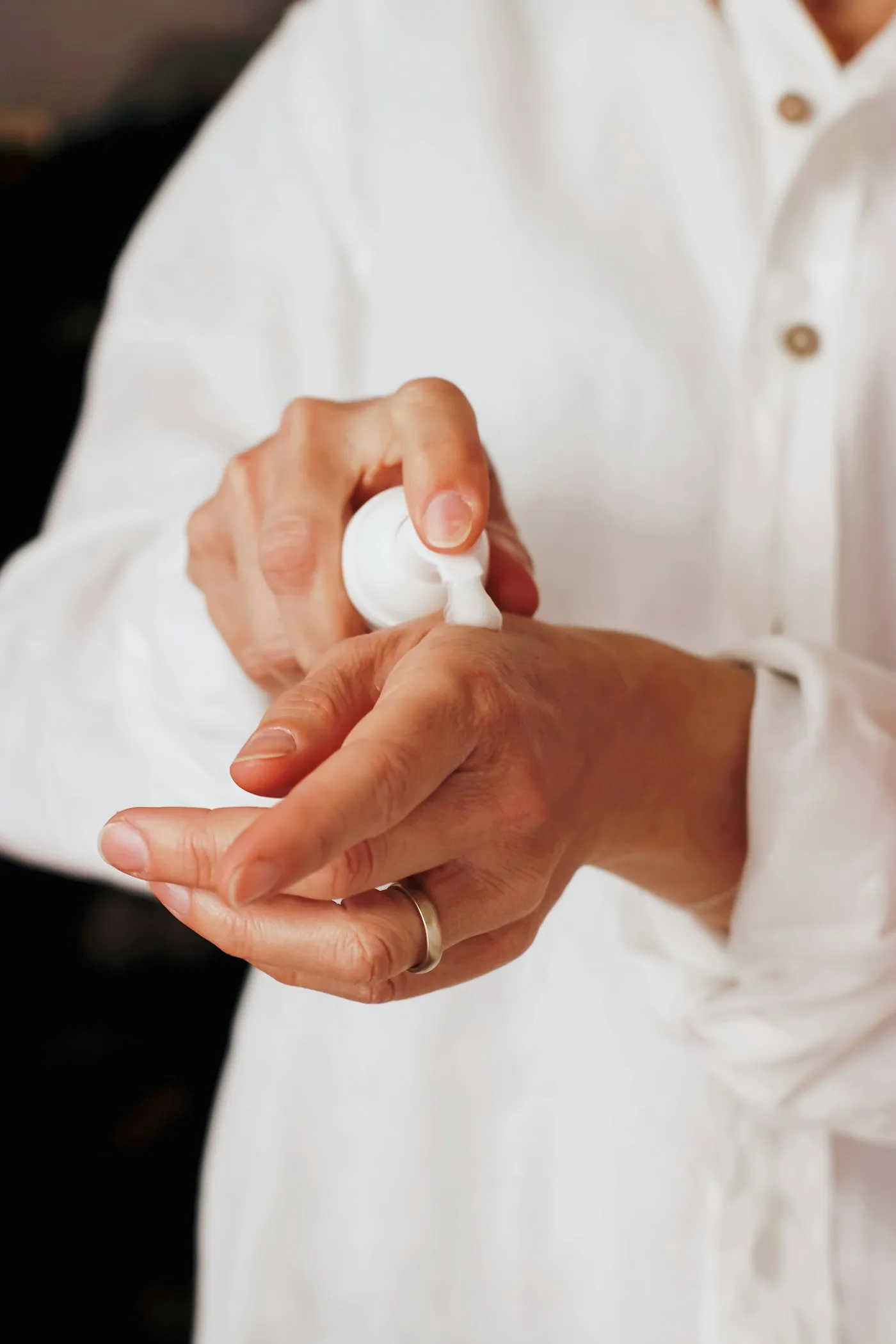 Manos aplicando crema de un dosificador blanco
