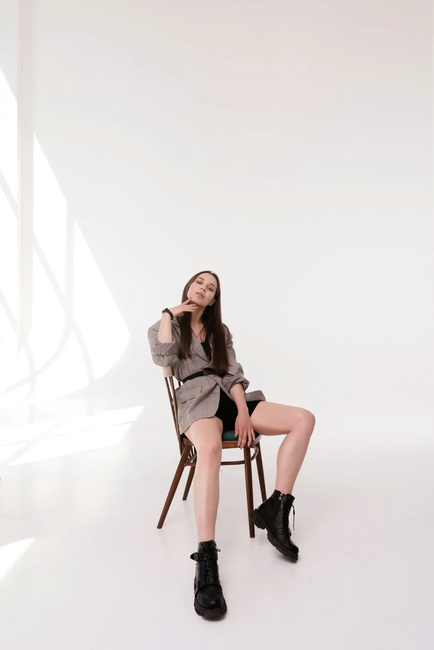 Modelo sentada en una silla de madera en un estudio blanco, con botas y vestido corto