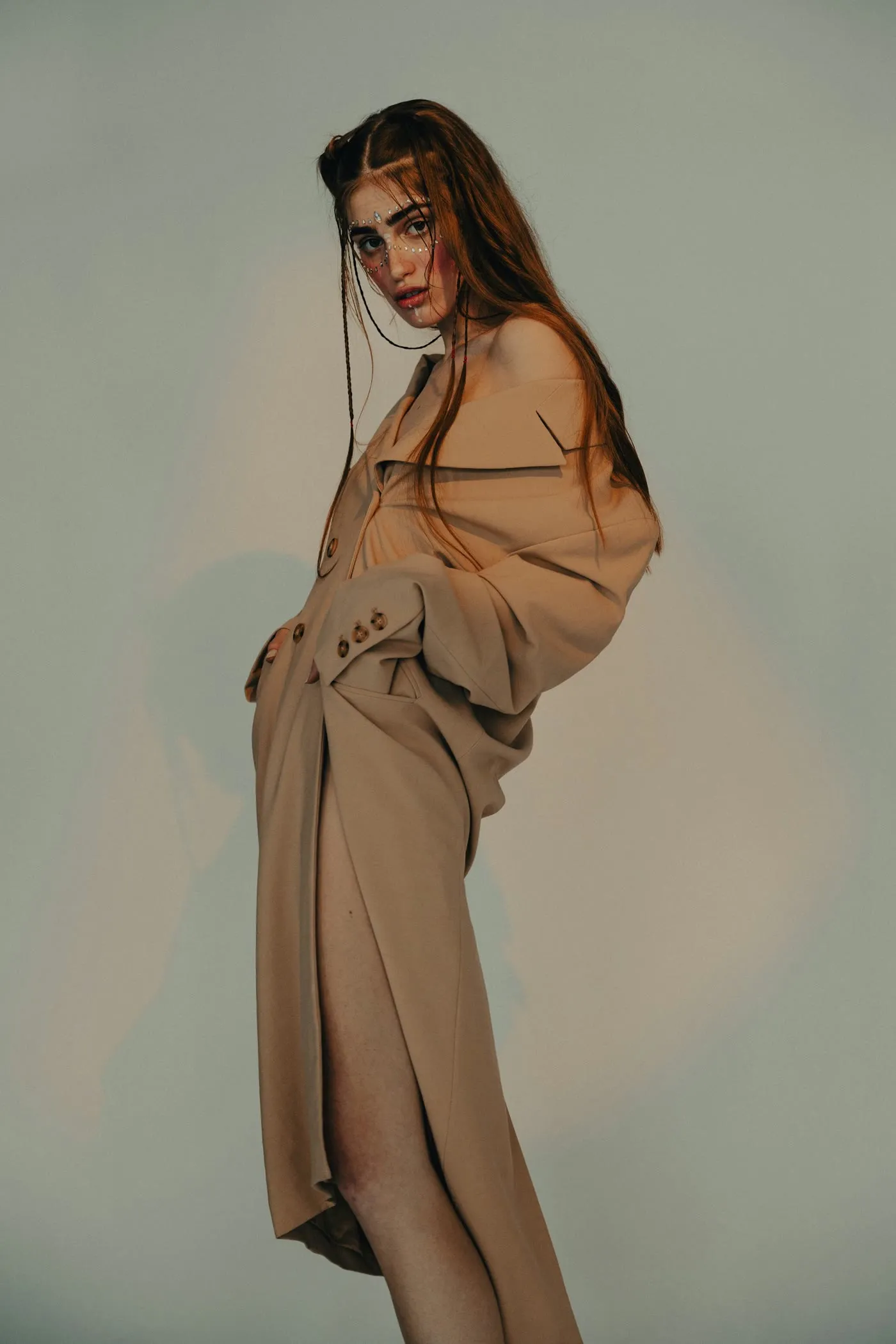 Modelo de pie con un abrigo largo, de perfil, en un estudio de fondo verde grisáceo